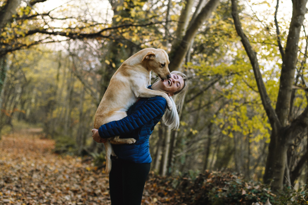 Pet Therapy: approcci e benefici degli amici a 4 zampe; Cane di media taglia in braccio ad una donna che ride divertita in un bosco. 
